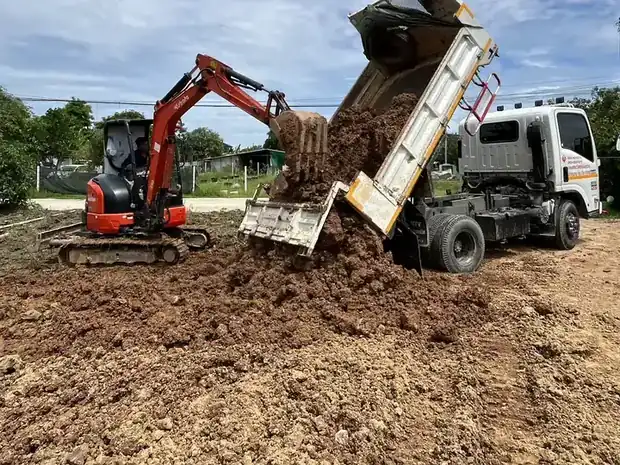 รถบรรทุกเทดินลงหน้างาน มีรถขุดรออยู่ข้าง ๆ